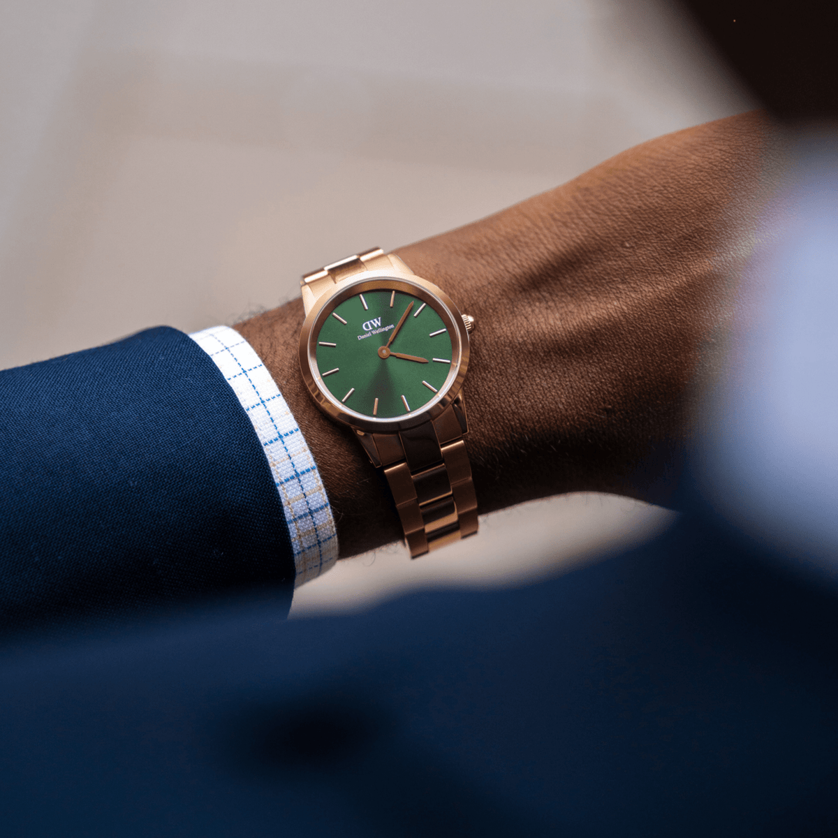 The Iconic Link Emerald Green Rose Gold watch is worn on the wrist, featuring a polished rose gold stainless steel bracelet and a striking emerald green dial, styled with formal business attire.