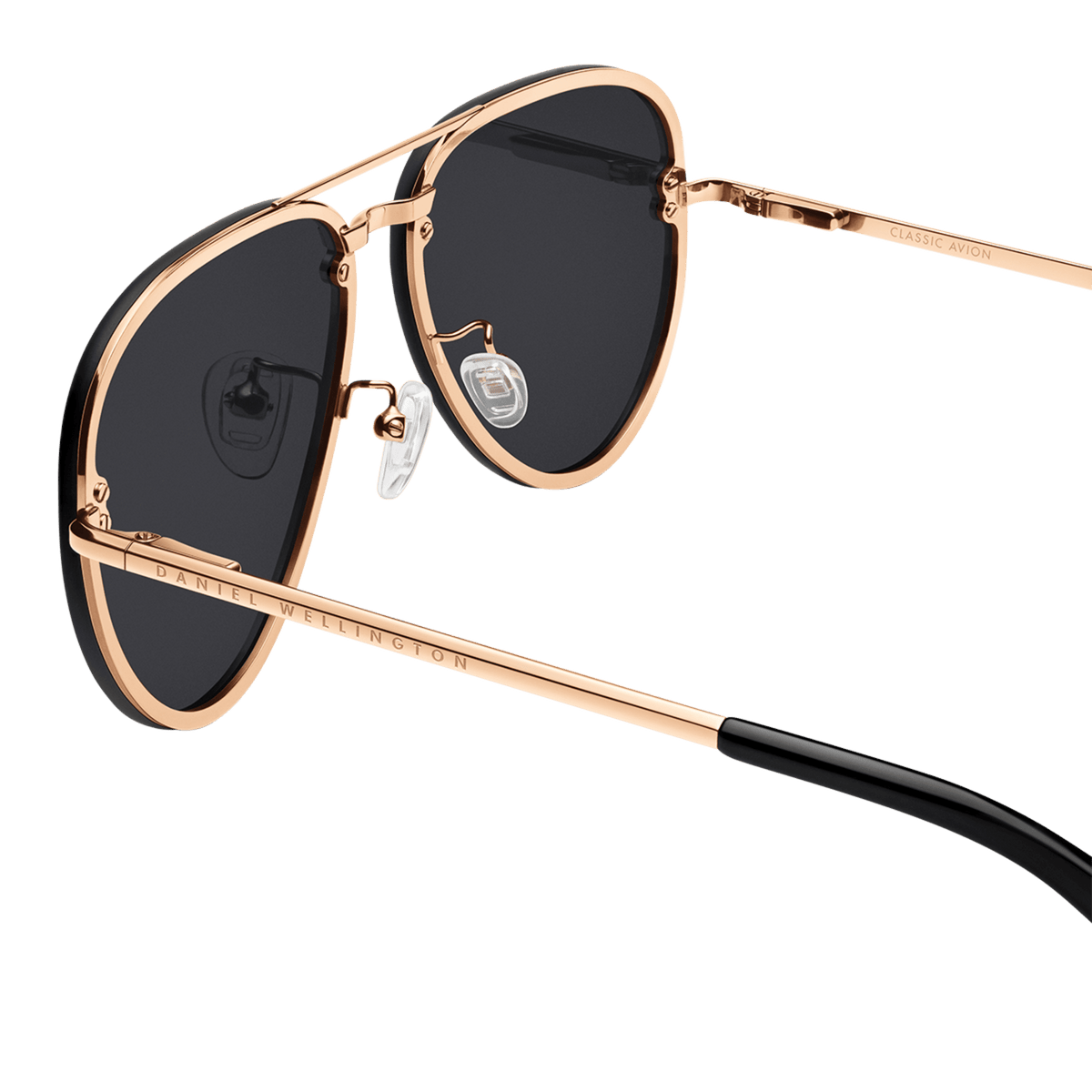Close-up of Avion Steel Rose Gold sunglasses highlighting the rose gold plated stainless steel frame, black aviator lenses, adjustable silicone nose pads, and Daniel Wellington branding on the arm.