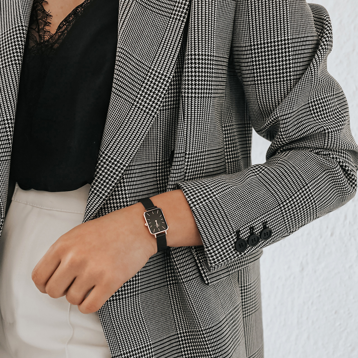 A woman wearing the Quadro Pressed Ashfield rose gold watch with a black mesh strap, styled with a checked blazer and black lace top for a smart, modern look.