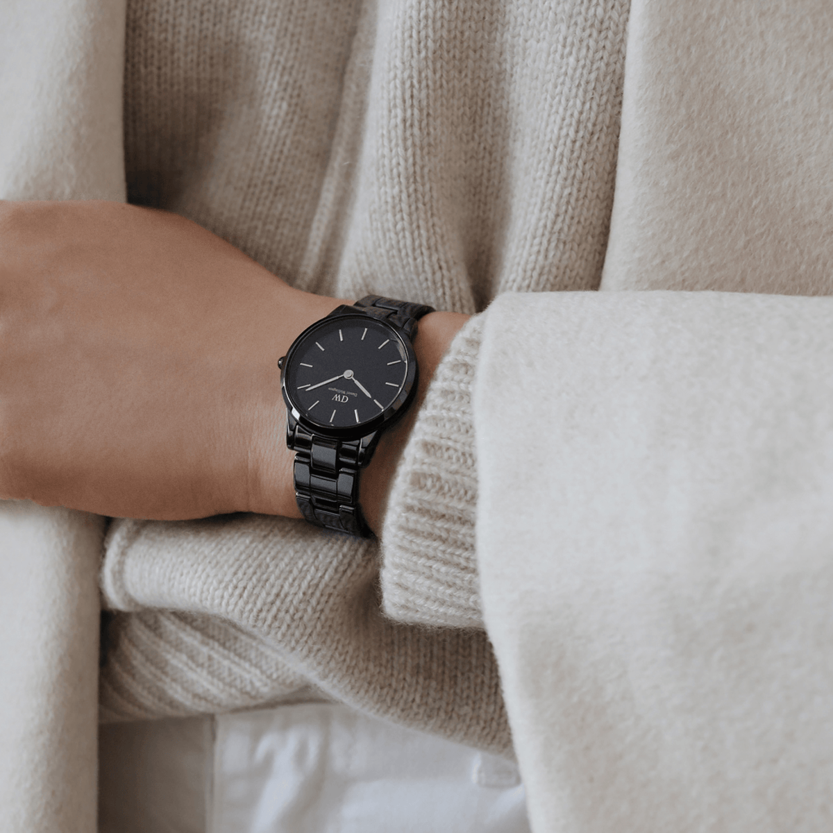 A woman wears the Iconic Link Ceramic watch with a glossy black ceramic bracelet and minimalist black dial, styled with a neutral knit and coat for a modern, everyday look.
