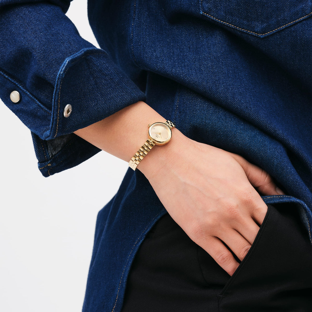 Elan Lumine Unitone Gold ladies watch with a slim gold bracelet and crystal dial, worn on the wrist with a denim shirt and black trousers, highlighting its versatile and elegant style for everyday wear.