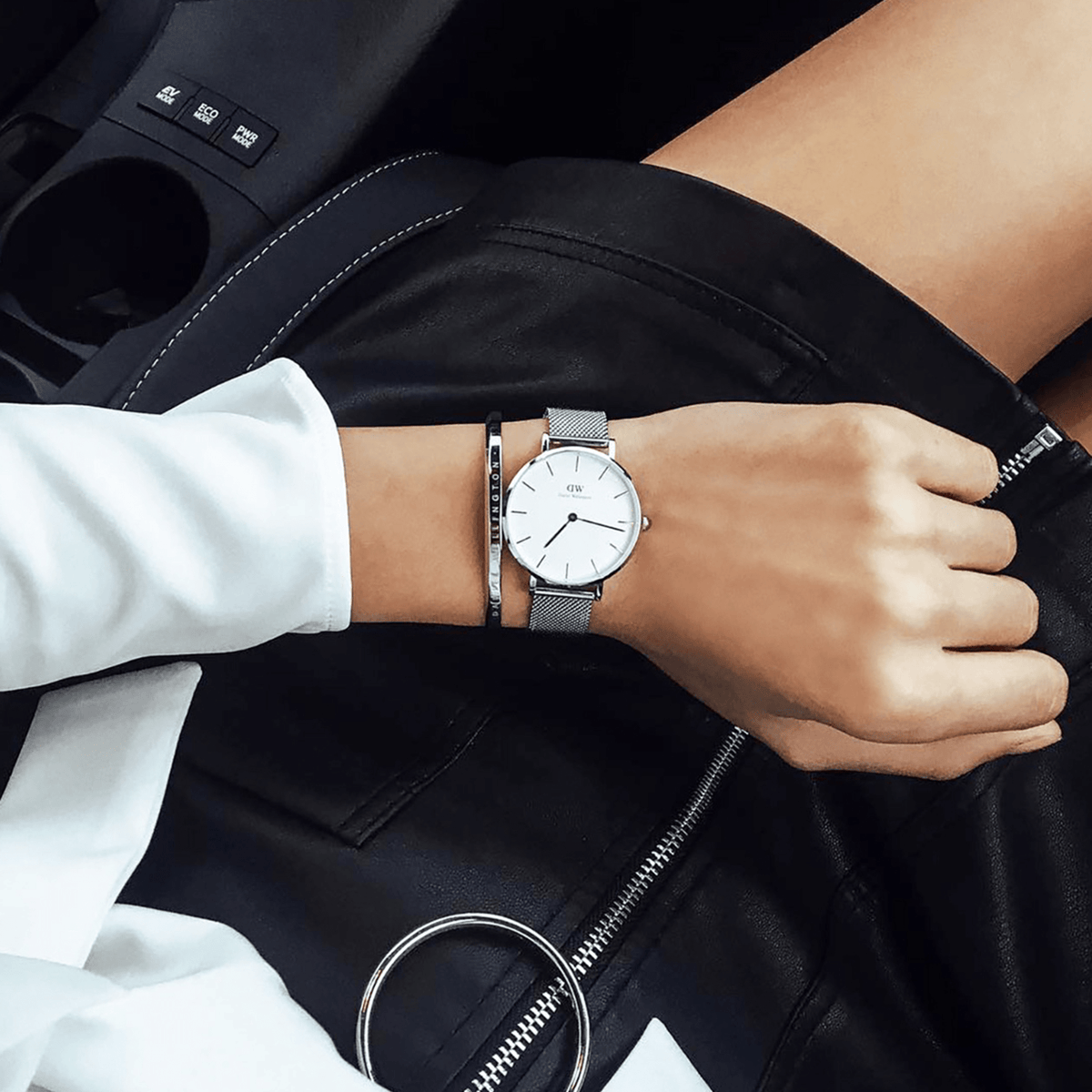 Petite Sterling Silver watch with a minimalist white dial and stainless steel mesh strap, worn alongside a silver bracelet for a stylish, modern look in a casual setting.