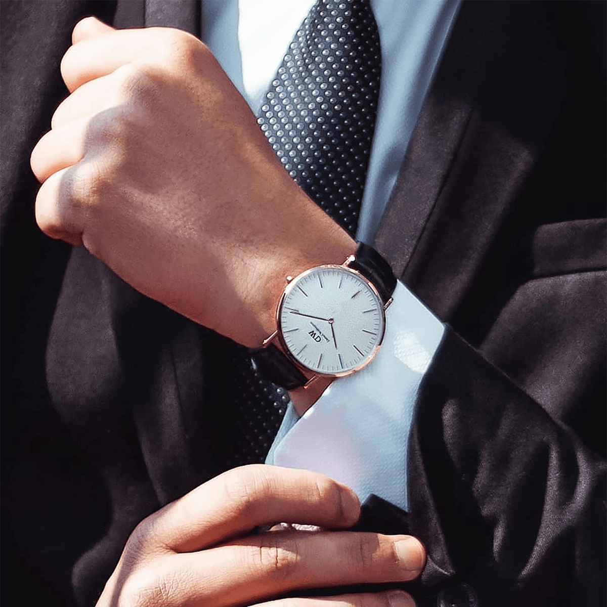 A man in a suit wears the Classic Sheffield Rose Gold watch, featuring a slim rose gold case, minimalist white dial, and black leather strap, styled for a polished business look.
