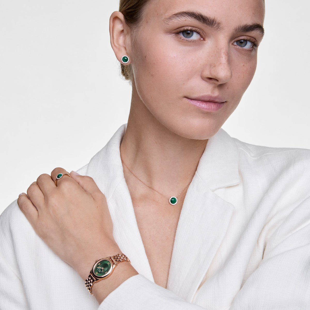A woman wears the Audrey Earrings Malachite Rose Gold, featuring round green malachite studs with a halo of white cubic zirconia set in rose gold, styled with matching jewellery for a coordinated and elegant look.