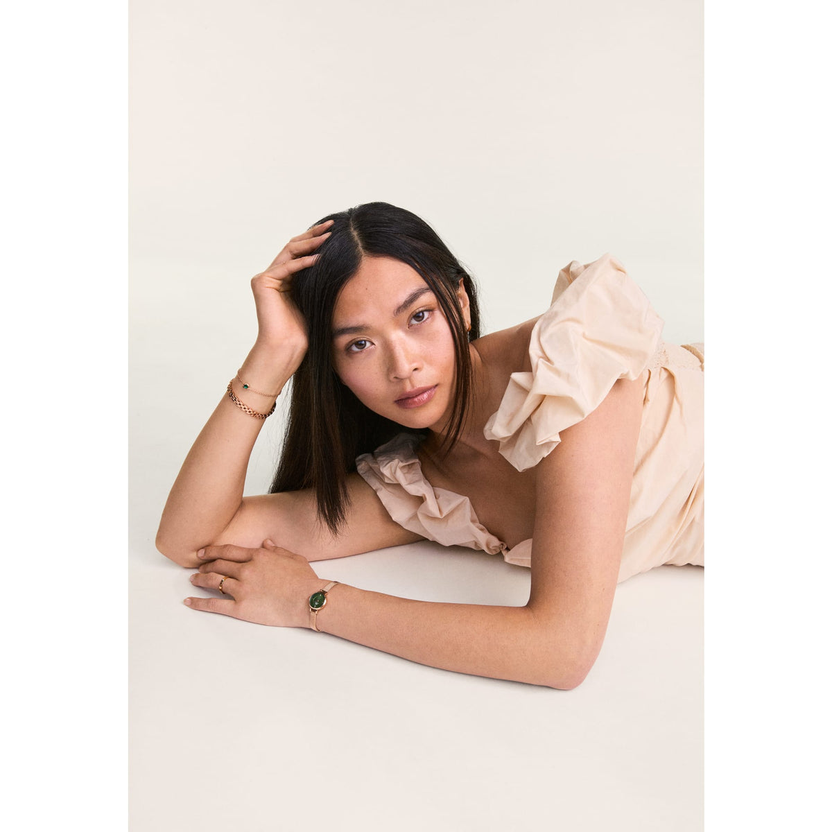 Woman wearing the Petite Mini Emerald Melrose watch with an emerald green dial and rose gold mesh strap, styled with a light ruffled dress and matching jewellery in a relaxed, elegant setting.