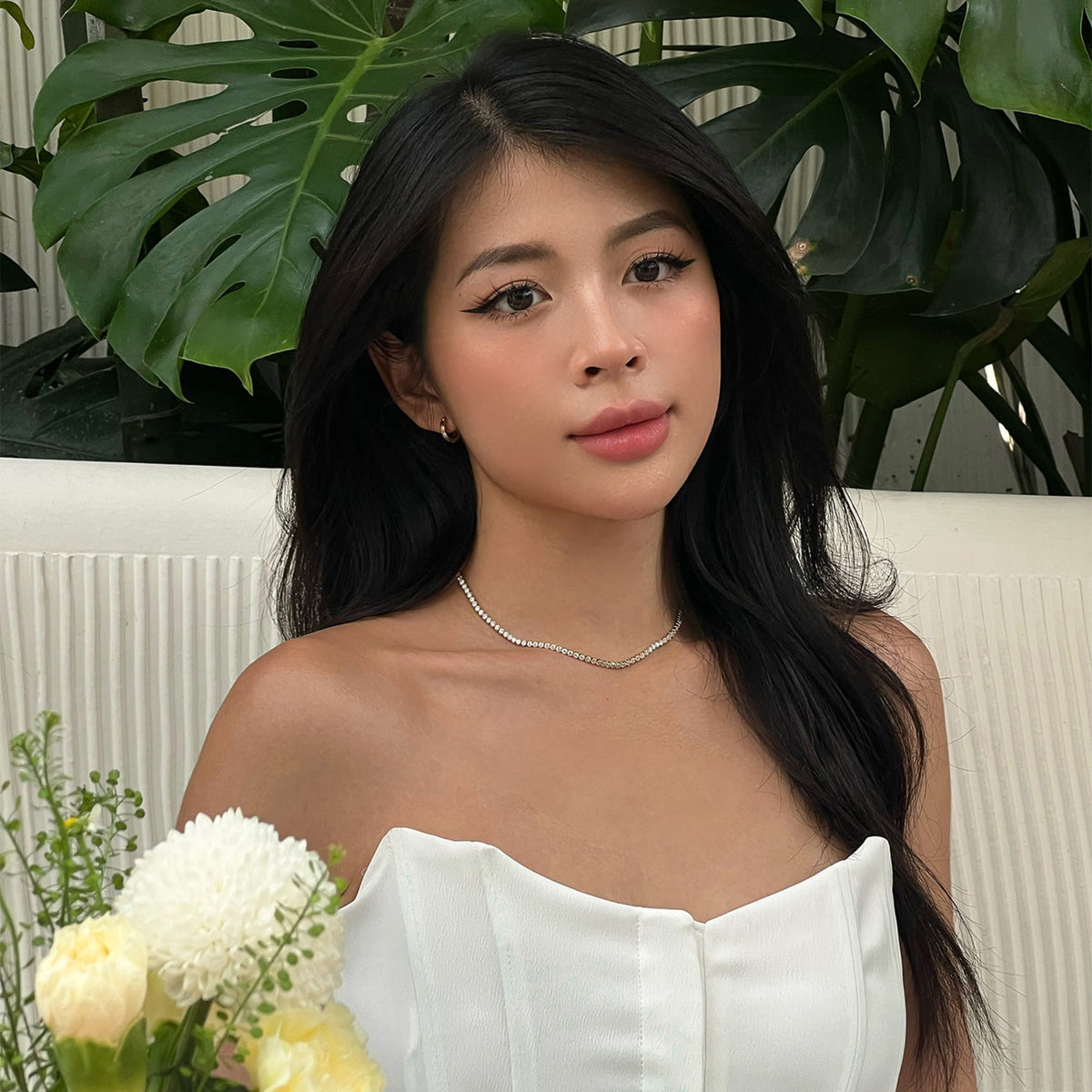 Classic Tennis Necklace Gold worn with a strapless white dress, featuring sparkling crystals and a delicate gold chain, styled for a special occasion with a bouquet of flowers.