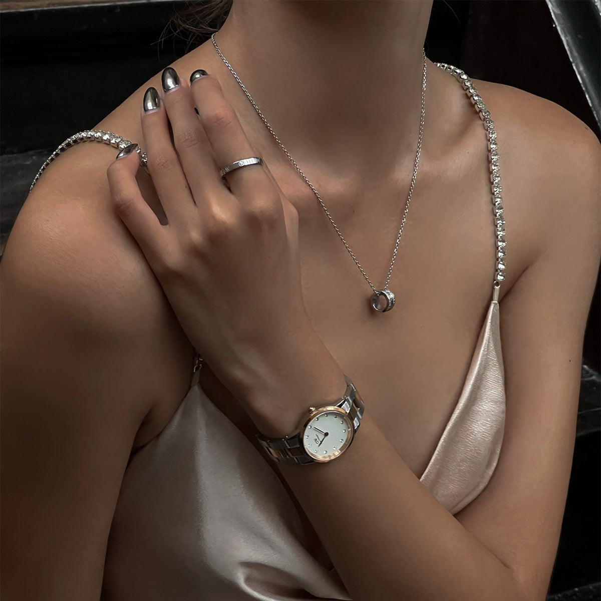 Woman wearing the Iconic Link Lumine Rose Gold watch with a two-tone rose gold and silver bracelet, eggshell white dial, and crystal hour markers, styled with silver jewellery and a satin dress for an elegant evening look.