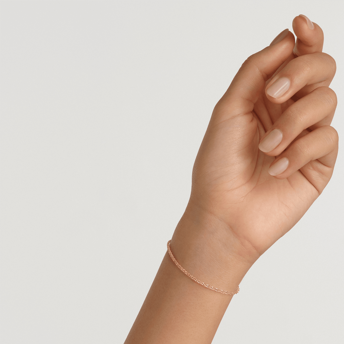 A woman’s wrist wearing the Twisted Chain Bracelet G, showing its slim twisted gold chain design and delicate fit, ideal for everyday elegance and layering with other jewellery.