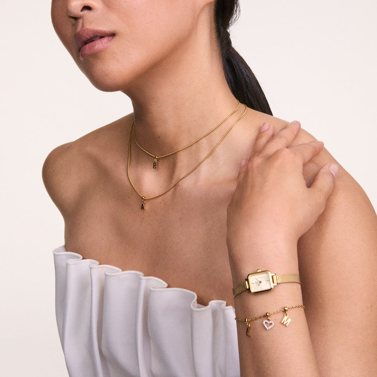 A woman wearing the Quadro Mini Evergold Champagne gold watch with a rectangular case and champagne dial, styled alongside a gold charm bracelet and layered gold necklaces, highlighting its elegant fit for petite wrists and versatility for both casual and formal outfits.