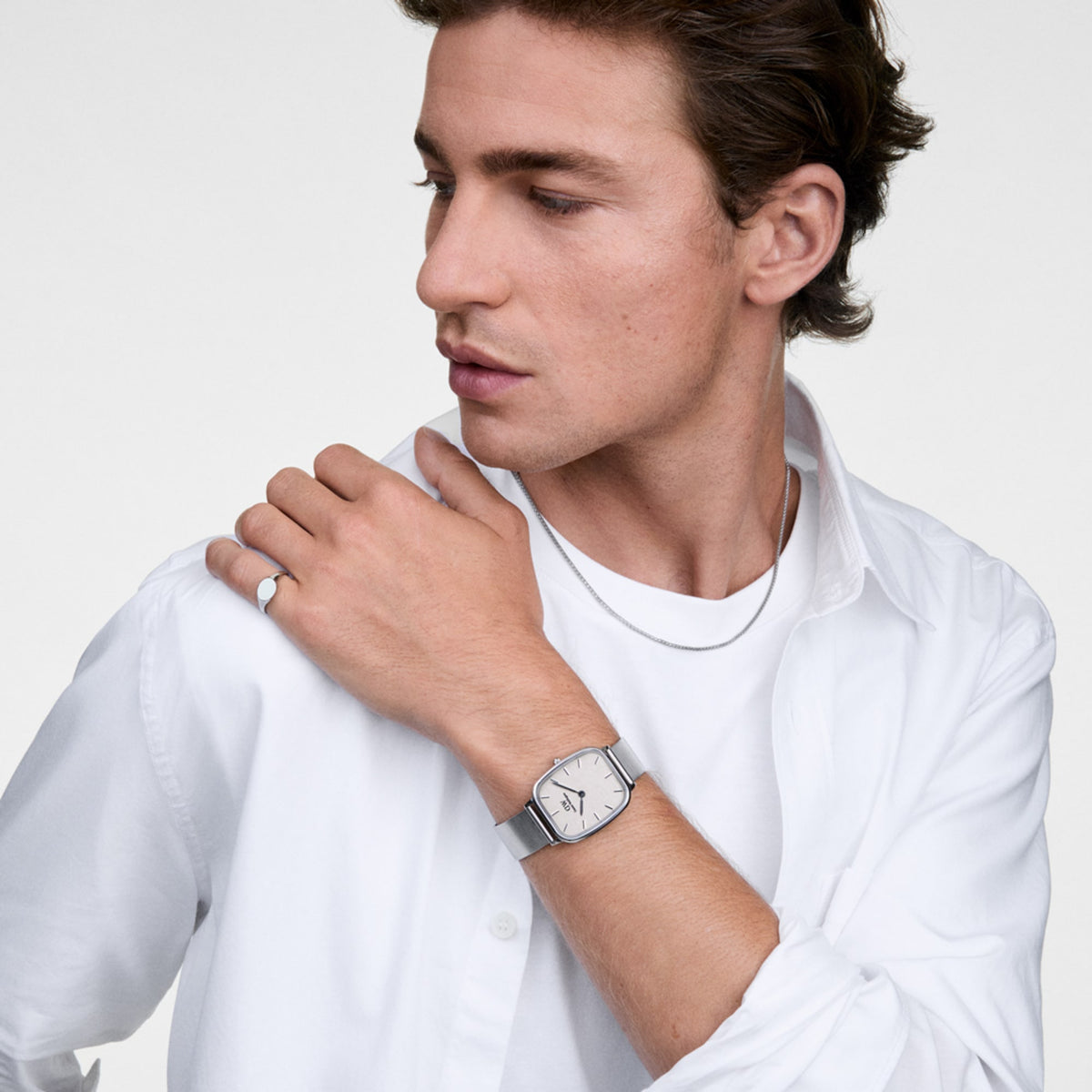 A man wearing the Classic Signet Ring Silver on his finger, styled with a silver watch, chain necklace, and a white shirt for a clean, modern look.