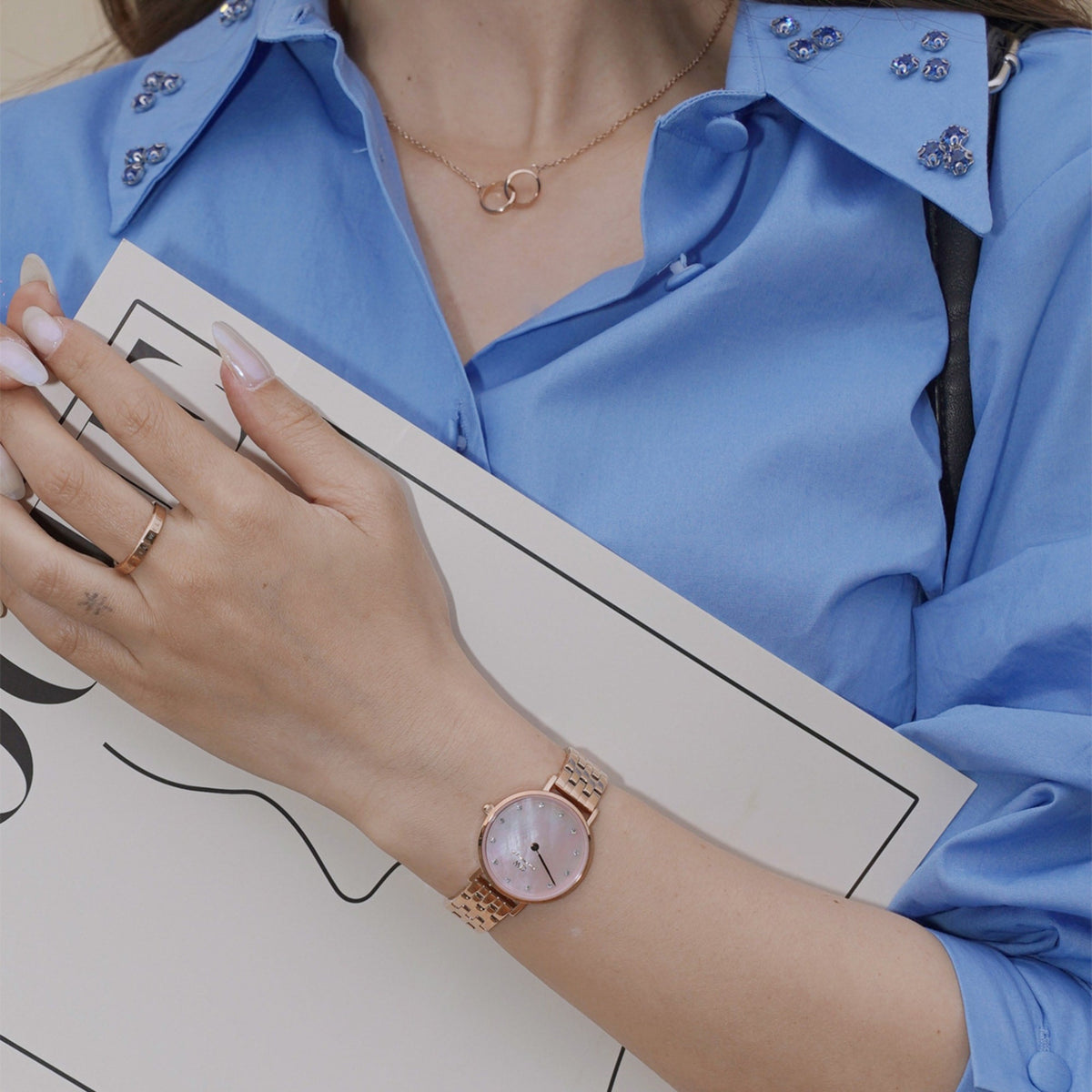 Woman wearing the Petite Lumine 5 Link Melrose Pink MoP Rose Gold watch with a rose gold bracelet and pink mother of pearl dial, styled with a blue shirt and rose gold jewellery for a polished everyday look.