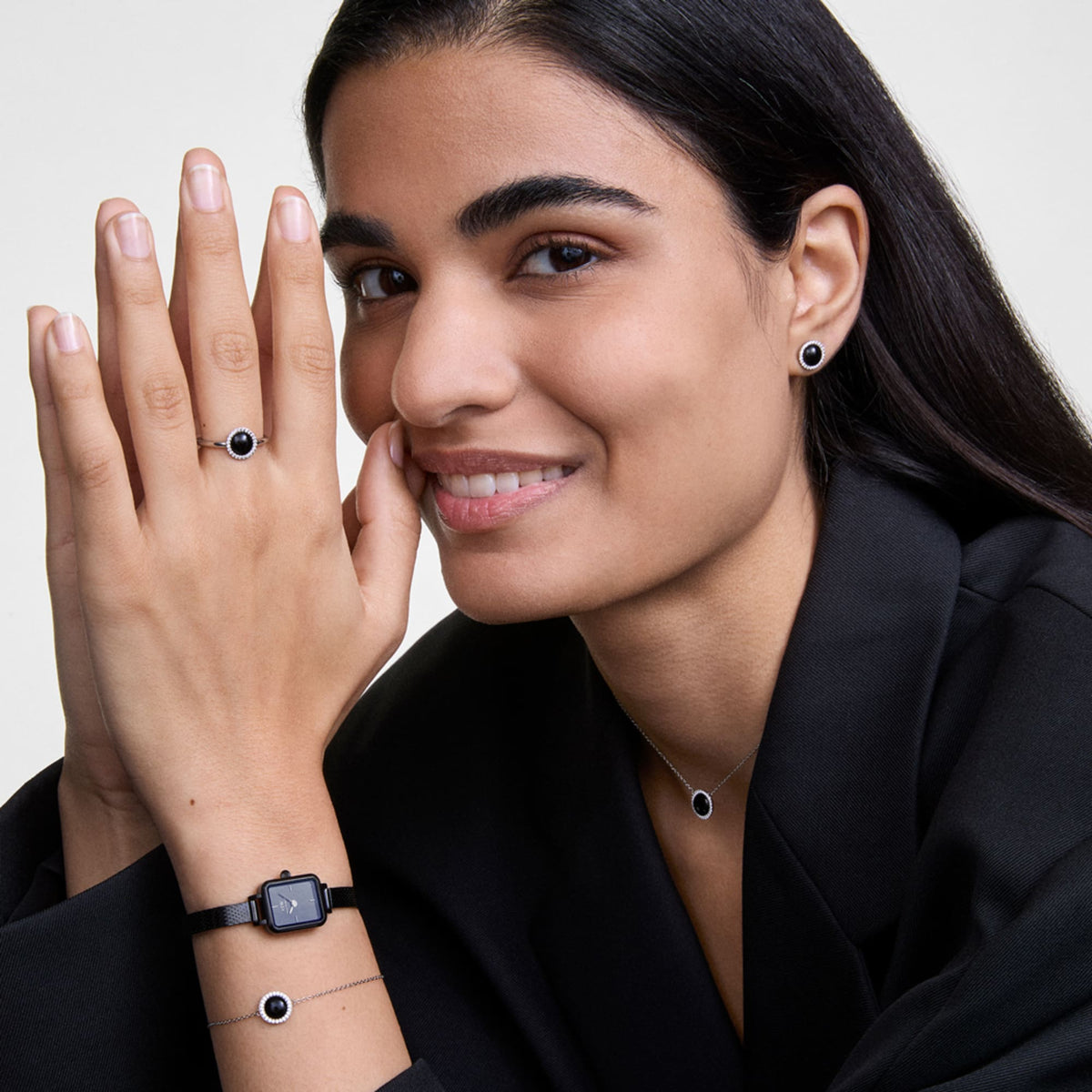 Quadro Mini Reflection Black watch with a rectangular mirror-effect black dial and slim mesh strap, styled on a woman's wrist alongside matching black jewellery for a modern, coordinated look.