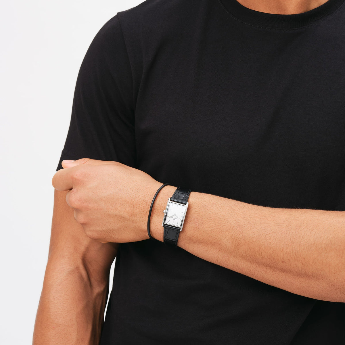 A man wearing the Sheffield Bracelet Silver alongside a black leather watch, showing the slim black leather band and polished silver clasp styled for a modern, coordinated look with casual attire.