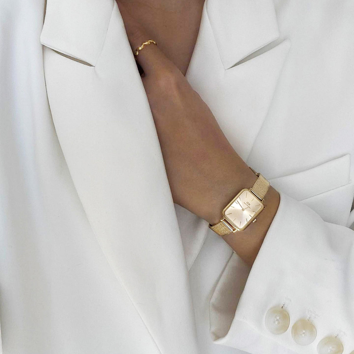 Quadro Pressed Unitone Gold watch with a rectangular gold dial and pressed mesh strap, styled with a white blazer for a polished, modern look.