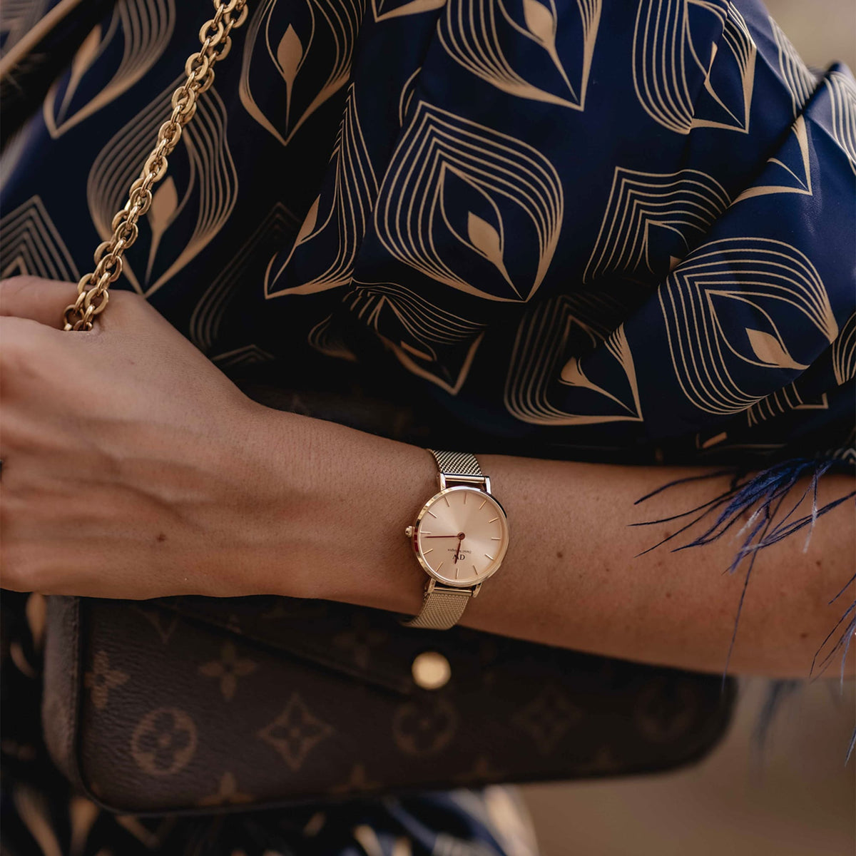 Petite Unitone Rose Gold watch with a rose gold mesh strap worn on a woman's wrist, styled with a patterned blouse and a gold chain handbag for a sophisticated, everyday look.