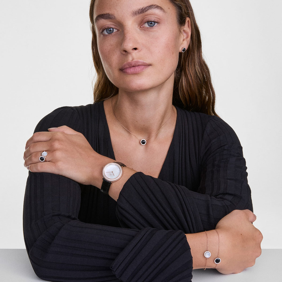 A woman wearing the Audrey Necklace Black Agathe Rose Gold, featuring a round black agate pendant with a halo of white cubic zirconia crystals on a rose gold chain, styled with matching jewellery and a black outfit for a sophisticated, coordinated look.