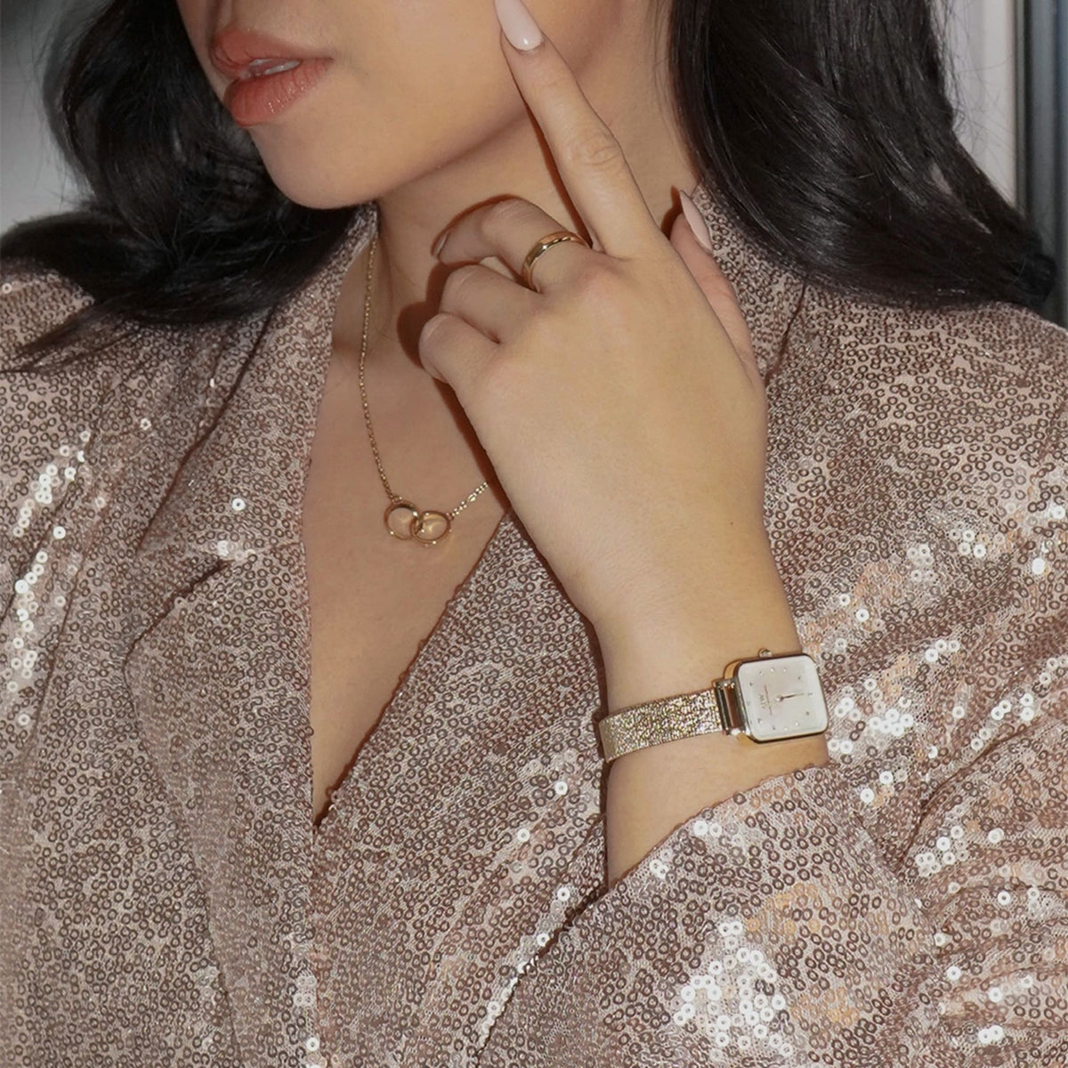A woman wearing the Elan Unity Necklace Gold with two interlocked rings on a fine gold chain, styled with a sequined outfit and matching gold accessories for a sophisticated, modern look.
