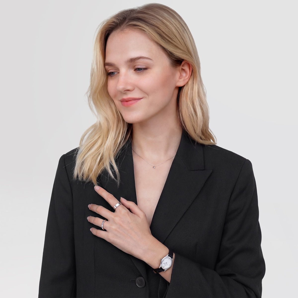 A woman wearing the Ophelia Mini Black Lizard White Guilloché Silver watch styled with a tailored black blazer, showing the petite oval dial and textured black leather strap paired for a modern, elegant look.