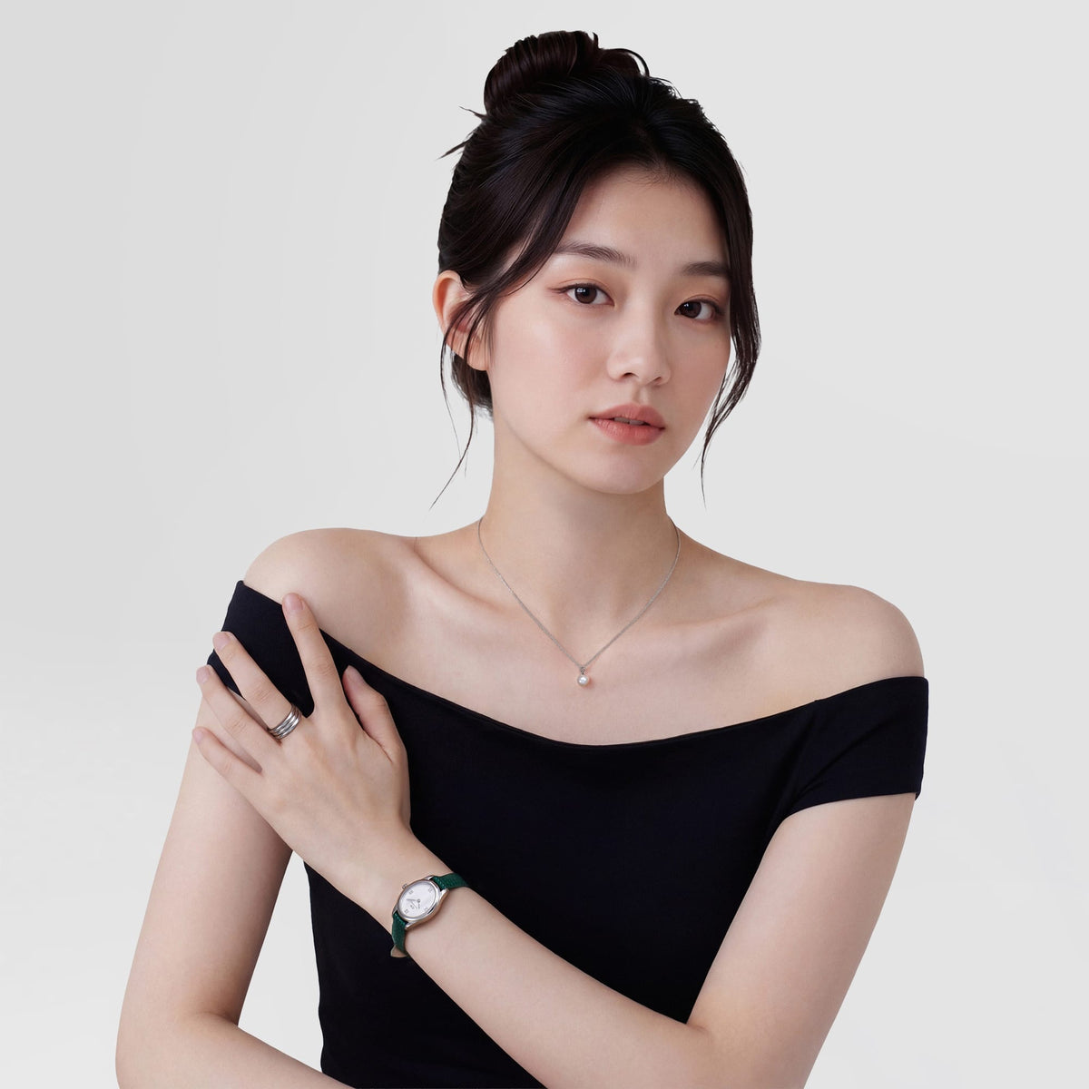 A woman wearing the Daniel Wellington Ophelia Mini Green Lizard White Guilloché Silver watch, styled with a green lizard-embossed leather strap and a petite oval silver case, paired with a black off-shoulder top and delicate jewellery for an elegant, modern look.