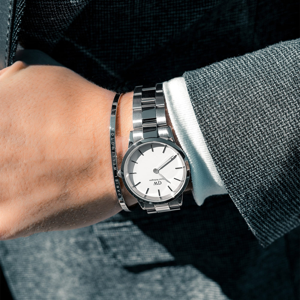 Iconic Link Silver watch by Daniel Wellington worn with a matching silver bracelet, featuring a minimalist eggshell white dial and polished stainless steel strap, styled with a formal suit for a refined business look.