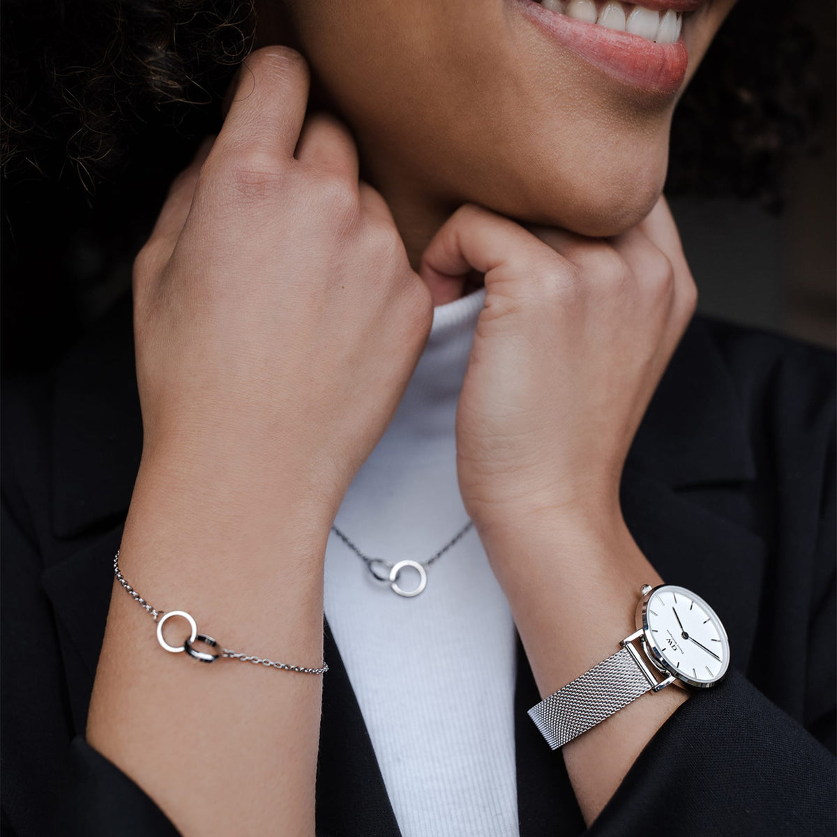 A woman wearing the Petite Sterling Silver watch with a slim stainless steel mesh strap, paired with a silver bracelet and necklace, styled for a modern and elegant everyday look.