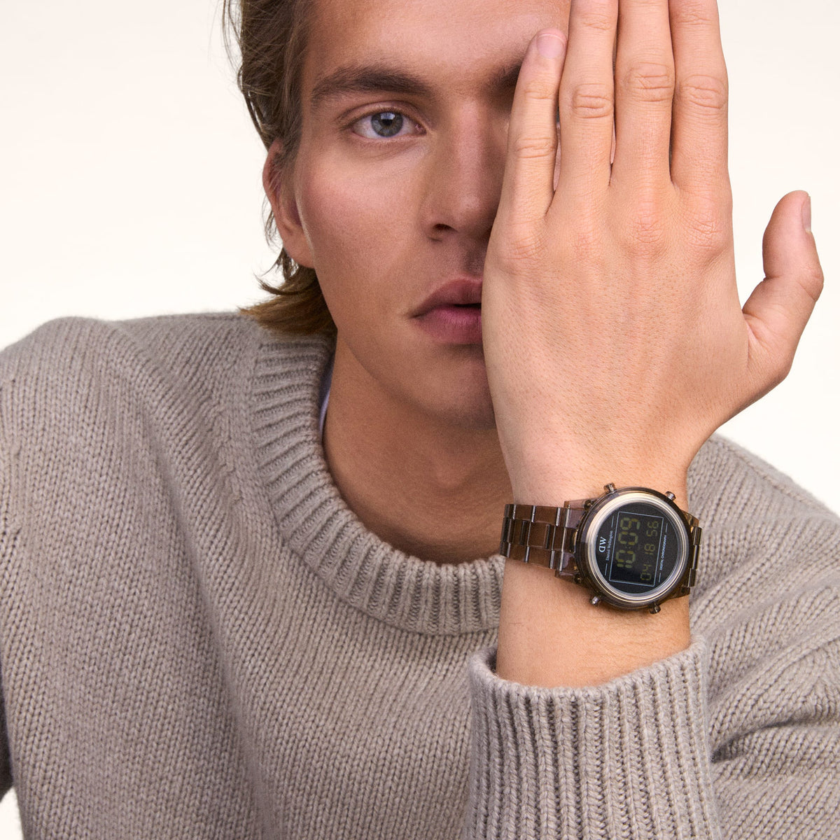 Daniel Wellington Retro Digital Dark Brown Dark Brown watch worn on the wrist, featuring a transparent dark brown link strap and round digital display, styled with a beige knitted jumper for a modern casual look.