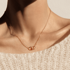 The Elan Unity Necklace Rose Gold worn at the collarbone, featuring two interlocking rose gold rings on a fine chain, styled with a soft knit top for an elegant everyday look.