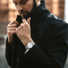 Iconic Link Silver watch by Daniel Wellington worn on the wrist with a black textured coat, showcasing its polished stainless steel bracelet and minimalist eggshell white dial in a stylish outdoor setting.