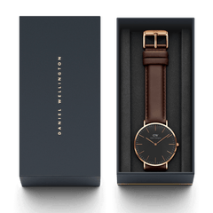 Classic Bristol Black Rose Gold watch with a black dial, rose gold case, and dark brown leather strap, presented in a Daniel Wellington branded gift box.