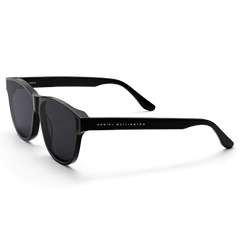 Ambler Bio-Acetate Black sunglasses with a sleek all-black Italian bio-acetate frame, dark UV400 lenses, and the Daniel Wellington logo subtly displayed on the arm.