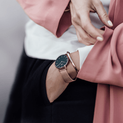 Petite Melrose Black Rose Gold watch with a black dial and rose gold mesh strap worn on a woman's wrist, styled with a rose gold bracelet and a pink blazer for a modern, elegant look.