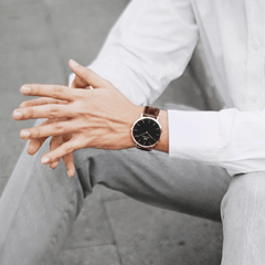 A person wearing the Classic Bristol Black Rose Gold watch with a black dial, rose gold case, and dark brown leather strap, styled with a white shirt and light trousers for a smart, everyday look.
