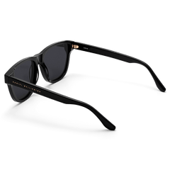 Ambler Bio-Acetate Black sunglasses with a modern classic shape, featuring a glossy black Italian bio-acetate frame, dark UV400 lenses, and the Daniel Wellington logo on the arm.