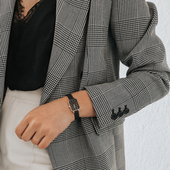 A woman wearing the Quadro Pressed Ashfield rose gold watch with a black mesh strap, styled with a checked blazer and black lace top for a smart, modern look.