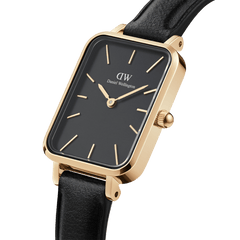 Quadro Pressed Sheffield Black Gold ladies watch with a rectangular gold stainless steel case, minimalist black dial, gold hour markers, and a slim black leather strap, shown in a close-up angled view.