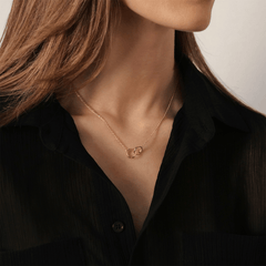 The Elan Unity Necklace Rose Gold with two interlocking rings on a fine chain, worn at the collarbone and styled with a black shirt for a modern, elegant look.