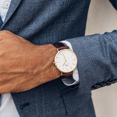 A man wearing the Classic Bristol Rose Gold watch with a slim rose gold case, minimalist white dial, and dark brown leather strap, styled with a blue suit for a polished, professional look.