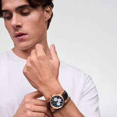 A man wearing the Iconic Chronograph Sheffield Arctic Panda Rose Gold watch, featuring a deep blue dial with white sub-dials, rose gold case, and black leather strap, styled with a casual white T-shirt.