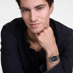 A person wearing the Tide Mesh Necklace Rose Gold 2.8, styled with a black shirt and paired with a gold mesh strap watch and gold ring for a modern, coordinated look.