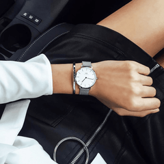 Petite Sterling Silver watch with a minimalist white dial and stainless steel mesh strap, worn alongside a silver bracelet for a stylish, modern look in a casual setting.