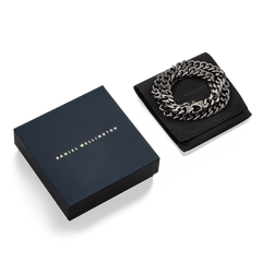 Ellipse Cuban Chain Necklace Graphite presented coiled on a black pouch next to a Daniel Wellington gift box, highlighting its bold links and matte graphite finish.