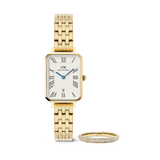 Rectangular gold women’s watch with a five-link bracelet, white dial, Roman numerals, blue hands, and date display, paired with a slim gold pavé ring set with sparkling crystals.
