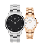Two Daniel Wellington Iconic Link watches displayed side by side, featuring a silver watch with a black dial and a rose gold ladies watch with a white dial, both with steel link straps and minimalist design.