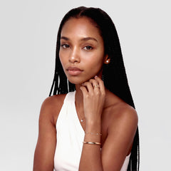 A woman wearing the Arch Cuff Rose Gold 6mm bracelet styled with other delicate jewellery, showcasing its polished rose gold finish and rounded profile as a modern accent to a white sleeveless top.