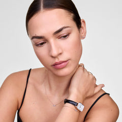 Quadro Roman Numerals Date Sheffield Rose Gold ladies watch worn on the wrist, featuring a rectangular rose gold case, white dial with Roman numerals, blue hands, date window, and a slim black leather strap styled with delicate jewellery.