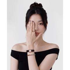 A woman wearing the Contrast Link Bracelet Two Tone Rose Gold on her wrist, styled with a black off-shoulder top and a watch, showcasing the bracelet’s polished silver and rose gold squared links for a modern, layered jewellery look.