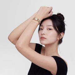 A woman wearing the Bound Mini Melrose rose gold watch with a rectangular case and mesh strap, styled with a delicate bracelet and a black top for a modern, elegant look.