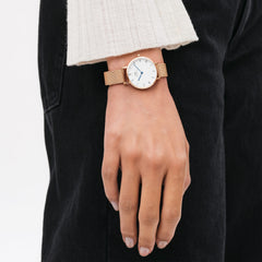 Petite Roman Numerals Melrose ladies watch with a rose gold mesh strap and white Roman numeral dial, worn on the wrist with casual black trousers and a cream knit top.