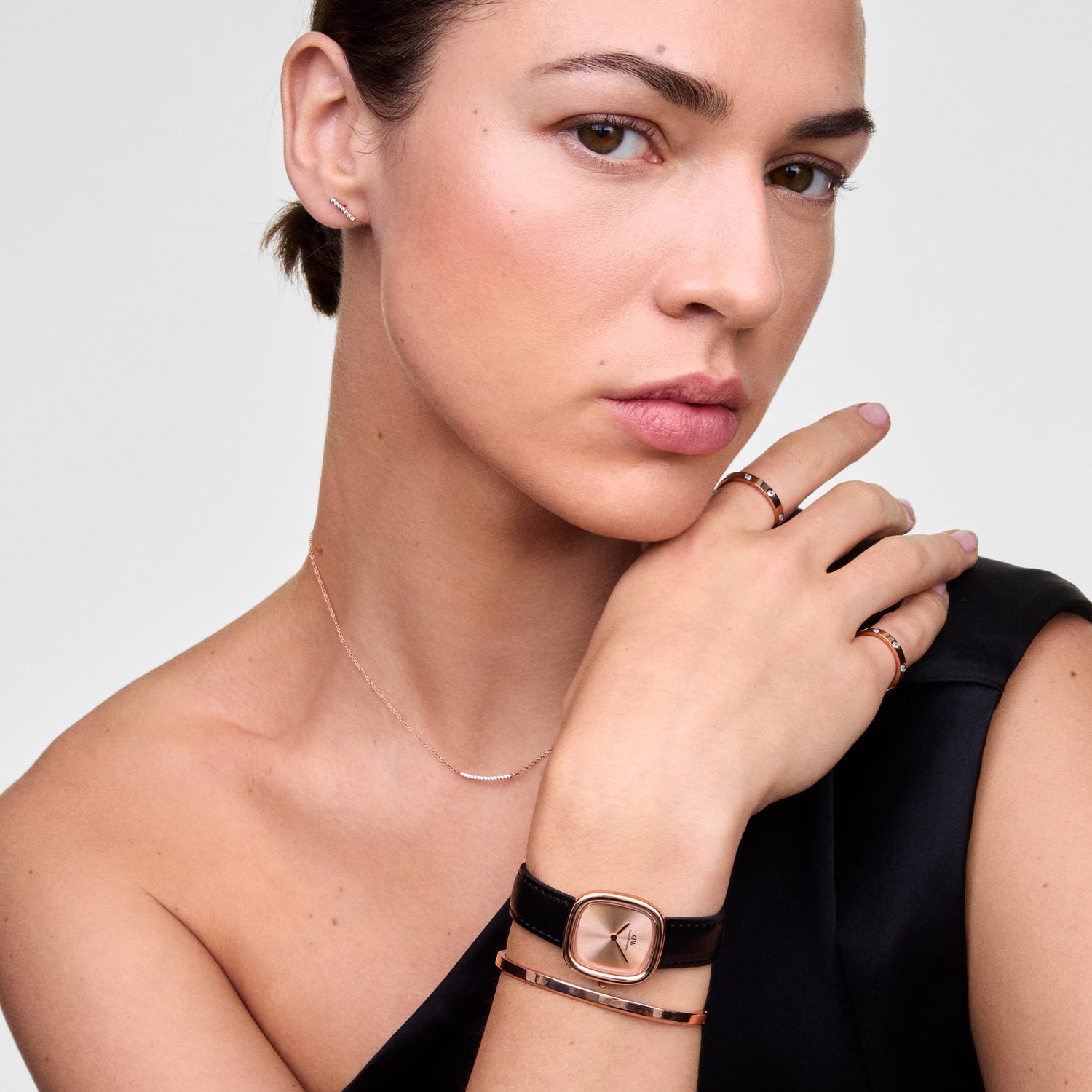 A woman wearing the Margot Sheffield Unitone Sunray Rose Gold ladies watch with a cushion-shaped rose gold case and minimalist dial, styled with a slim black leather strap and paired with rose gold jewellery for an elegant, modern look.