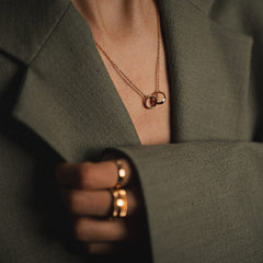 A woman wearing the Elan Unity Necklace Rose Gold with two interlocking rings on a fine chain, styled with a tailored blazer and matching rose gold rings for a sophisticated, modern look.